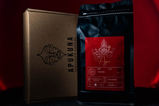 Bolsa de café Agni de Apukuna Coffee junto a una caja de cartón con el logotipo de la marca. Fondo rojo y empaque elegante que resalta la presentación premium del café de especialidad indio.
